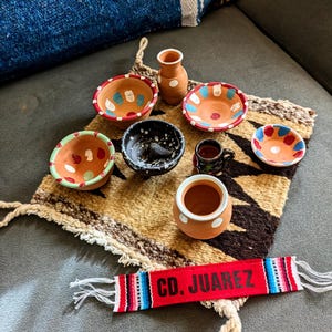 May include: A set of small, hand-painted terracotta pottery bowls and a vase, with a red and white woven band that says "CD. JUAREZ".