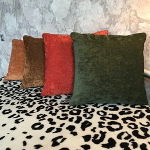 May include: Four decorative throw pillows with different colors and textures. The pillows are arranged in a row on a white and black animal print fabric.