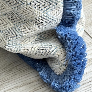 May include: A close-up of a throw pillow with a blue and white geometric pattern and a blue fringe border.