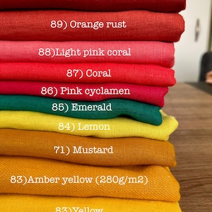 May include: A stack of folded fabric swatches in various colors labeled with numbers and names: 90) Rouge cherry, 89) Orange rust, 88) Light pink coral, 87) Coral, 86) Pink cyclamen, 85) Emerald, 84) Lemon, 71) Mustard, 83) Amber yellow (280g/m2), 83) Yellow.
