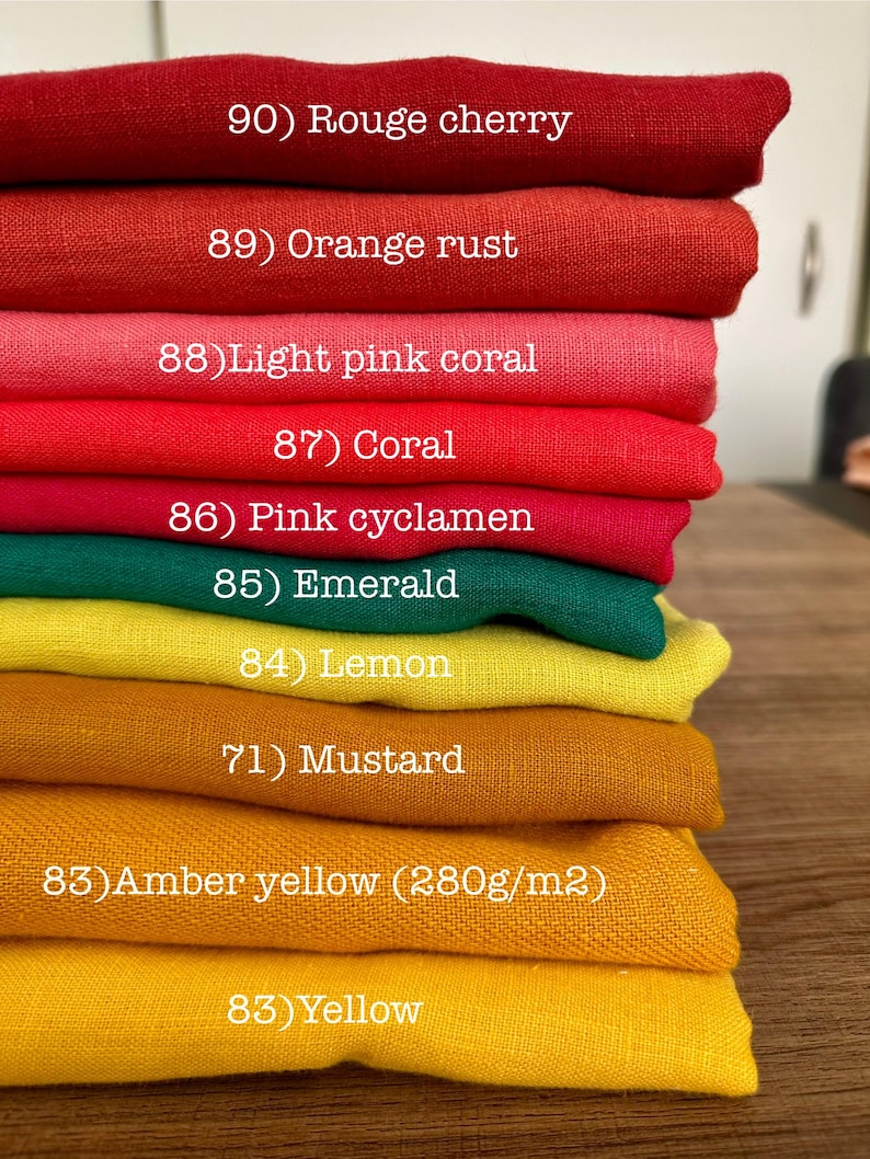 May include: A stack of folded fabric swatches in various colors labeled with numbers and names: 90) Rouge cherry, 89) Orange rust, 88) Light pink coral, 87) Coral, 86) Pink cyclamen, 85) Emerald, 84) Lemon, 71) Mustard, 83) Amber yellow (280g/m2), 83) Yellow.