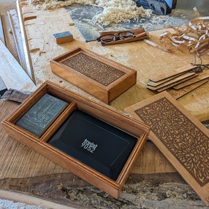 Two boxes are displayed: one with its lid removed, featuring an Ex Libris stamp and its accompanying stamp pad, with the other box sitting directly behind it, with its lid closed. In the foreground are tools, a pair of glasses, a stamp and sawdust.