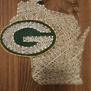 May include: String art of the state of Wisconsin with the Green Bay Packers logo in the center. The logo is green and yellow with a white "G" inside.