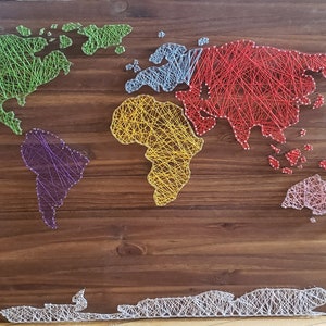 Könnte beinhalten: Eine Weltkarte aus String Art auf einem Holzgrund. Die Kontinente sind in verschiedenen Farben umrandet: grün, lila, gelb, blau und rot.