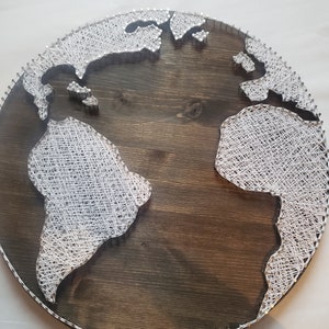 Könnte beinhalten: Eine runde Holzplatte mit einem weißen String-Art-Design der Weltkarte. Die Platte ist dunkelbraun und die Schnur ist weiß.