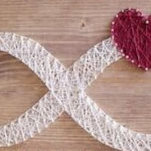 以下が含まれることがあります： 木製の表面に、釘に巻き付けられた白い糸で無限大の記号が作られています。無限大の記号の中央には赤いハートがあります。