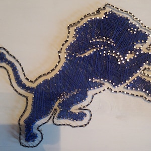 Puede incluir: Arte de hilo azul de un león, una mascota deportiva popular, sobre un fondo blanco.