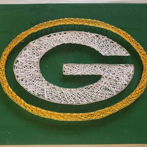 May include: A string art design of the letter "G" in white thread on a green background. The letter is outlined in yellow thread.