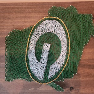 May include: Green and white string art depicting the Green Bay Packers logo, a stylized "G" inside a circle, on a wooden background.