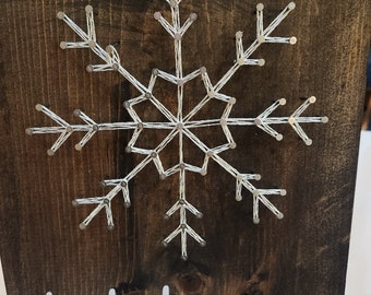 Peut inclure: Une pancarte en bois avec un flocon de neige en fil blanc et le texte "Let it snow" en lettres blanches.