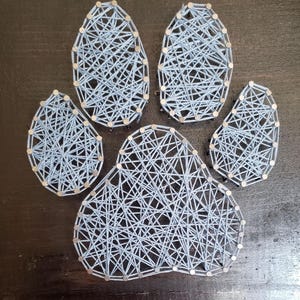 Può includere: Un design di impronta di zampa in filo blu chiaro. L'impronta è realizzata con chiodi e filo blu chiaro, creando un effetto strutturato. Il design è un simbolo di animali domestici e animali.