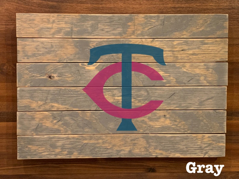 K&ouml;nnte beinhalten: Ein Holzschild mit einem grauen, blauen und rosafarbenen Minnesota Twins Logo. Das Schild ist aus wiederverwendetem Holz gefertigt und hat einen rustikalen Look.