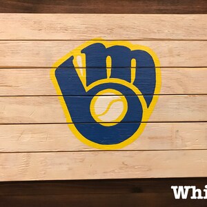 K&ouml;nnte beinhalten: Ein Holzschild mit einem bemalten Baseballhandschuh in Blau, Gelb und Wei&szlig;. Der Handschuh ist ein Logo f&uuml;r die Milwaukee Brewers.