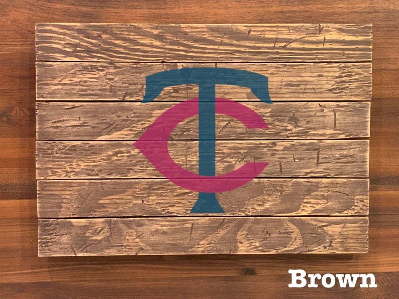 K&ouml;nnte beinhalten: Ein Holzschild mit einem stilisierten "TC"-Logo in Teal und Maroon. Das Schild ist aus wiederverwendetem Holz gefertigt und hat einen rustikalen, abgenutzten Look. Das Wort "Brown" ist unter dem Schild gedruckt.