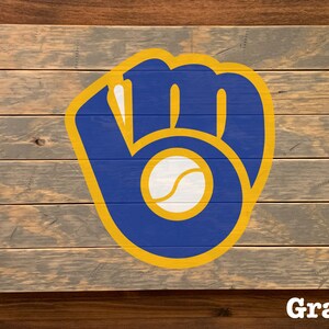 K&ouml;nnte beinhalten: Ein Holzschild mit einem blauen und gelben Baseballhandschuh-Logo. Das Logo enth&auml;lt einen wei&szlig;en Baseball. Das Schild ist grau gestrichen.