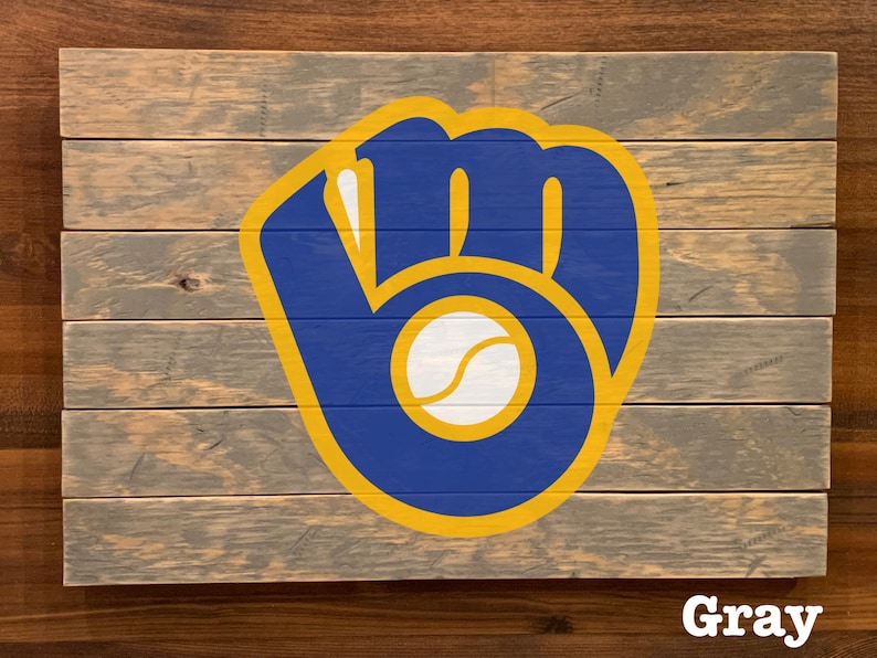 K&ouml;nnte beinhalten: Ein Holzschild mit einem blauen und gelben Baseballhandschuh-Logo. Das Logo enth&auml;lt einen wei&szlig;en Baseball. Das Schild ist grau gestrichen.
