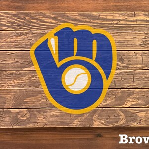 K&ouml;nnte beinhalten: Ein Holzschild mit einem blauen und goldenen Baseballhandschuh-Logo. Das Logo befindet sich auf einem braunen Holzgrund. Das Wort "Brown" ist unter dem Logo gedruckt.