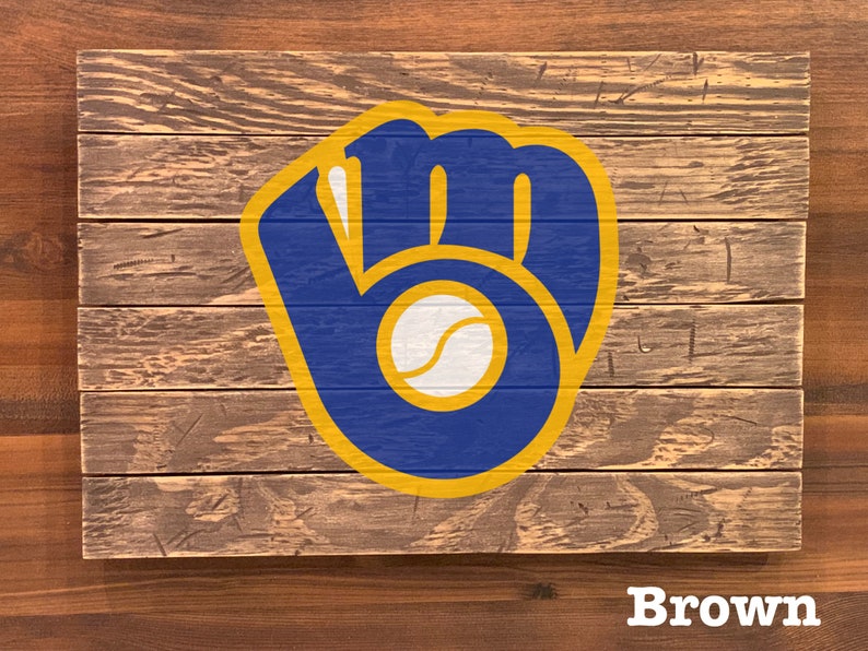 K&ouml;nnte beinhalten: Ein Holzschild mit einem blauen und goldenen Baseballhandschuh-Logo. Das Logo befindet sich auf einem braunen Holzgrund. Das Wort "Brown" ist unter dem Logo gedruckt.