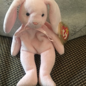 May include: Pink plush bunny with long floppy ears, a pink ribbon around its neck, and a Ty Beanie Baby tag attached to its ear.