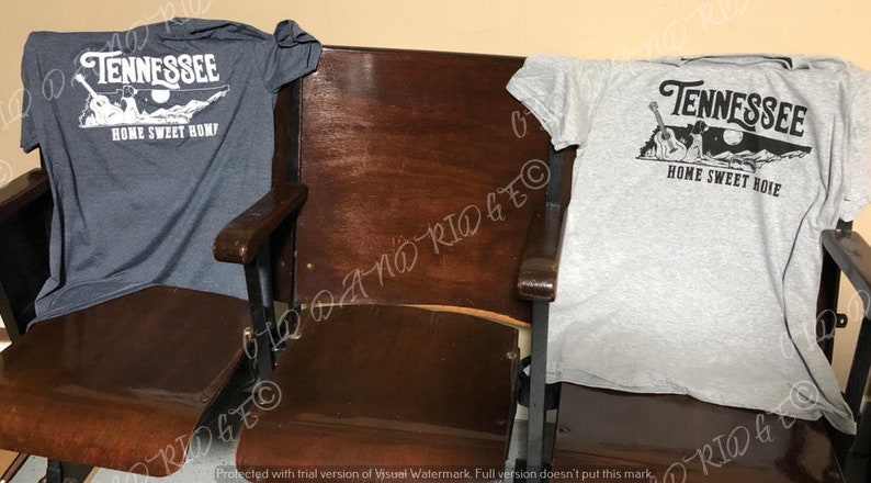 May include: Two t-shirts featuring a Tennessee state outline design. The shirts are grey and dark blue. The design includes a guitar, a moon, and the words "Tennessee" and "Home Sweet Home".