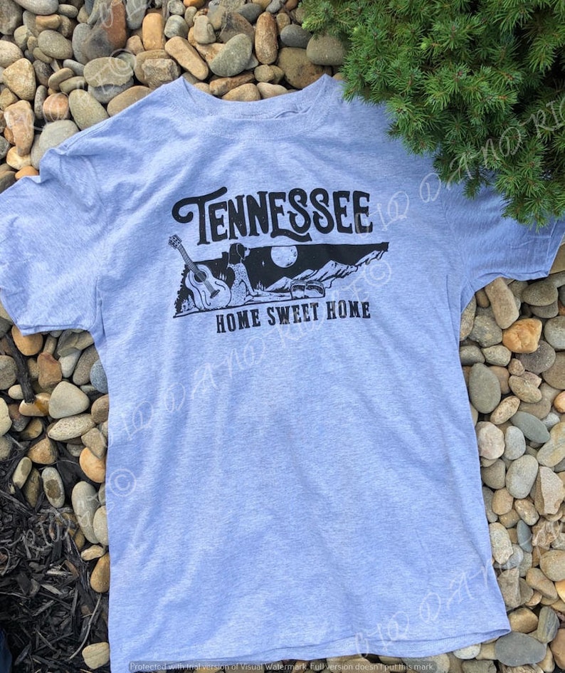 May include: A light blue t-shirt with a black graphic design featuring a guitar, a person, a mountain range, and the text "Tennessee Home Sweet Home".
