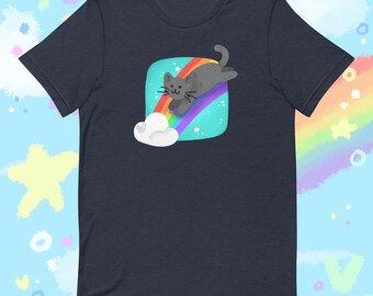 Op de afbeelding: Marineblauw T-shirt met een cartoon kat op een regenboog. De grijze kat rijdt op een veelkleurige regenboog, tegen een turquoise achtergrond met sterren en een witte wolk. Klassieke ronde hals.