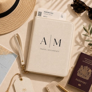 Puede incluir: Un organizador de documentos de viaje color crema con correa de muñeca, con las letras AM y el texto TRAVEL DOCUMENTS. Contiene una tarjeta de embarque para la puerta 23, asiento 12A. Cerca hay un sombrero de paja, gafas, un mapa y un pasaporte.
