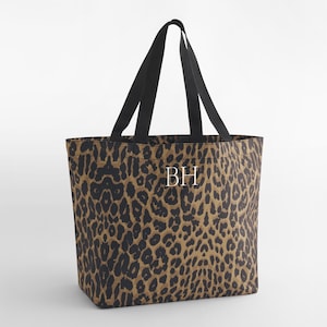 Puede incluir: Un bolso tote con estampado de leopardo en tonos marrón y negro. Tiene asas negras y las iniciales blancas "BH". Esta bolsa está diseñada para transportar objetos.