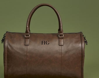 Può includere: Una borsa da viaggio in pelle marrone con una cerniera nera e un manico in pelle nera. La borsa ha le iniziali "HG" in rilievo sul davanti.