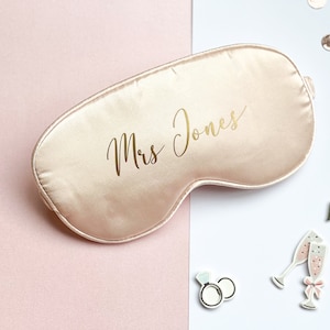 以下が含まれることがあります： ゴールドの文字で「Mrs. Jones」と書かれた、薄いピンクのサテン製のアイマスクです。