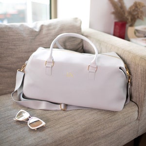 May include: A light gray leather travel bag with a gold zipper and gold hardware. The bag has a shoulder strap and the initials "LN" are embossed on the front.