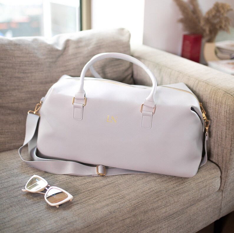 May include: A light gray leather travel bag with a gold zipper and gold hardware. The bag has a shoulder strap and the initials "LN" are embossed on the front.