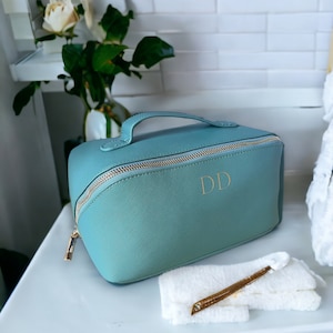 May include: A teal blue zippered travel makeup bag with a gold zipper and handle. The bag has the initials "DD" in gold lettering on the front.