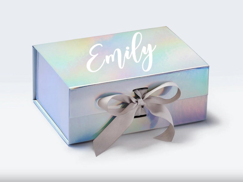 May include: A silver iridescent gift box with a gray satin ribbon and bow. The box has the name "Emily" printed on the top in white.