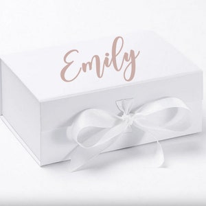 May include: White gift box with a white ribbon and bow. The box has the name "Emily" written on the top in a pink cursive font.