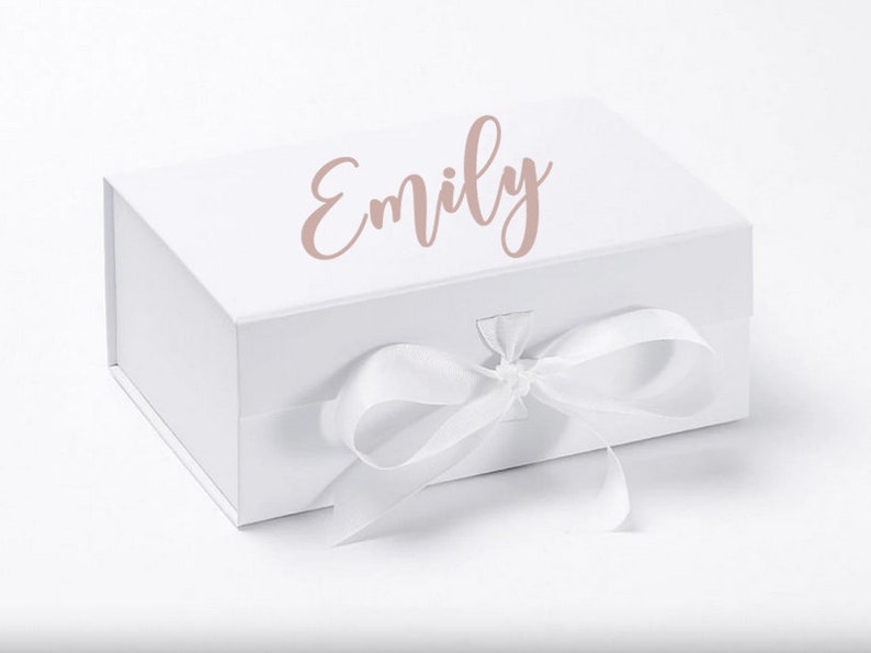May include: White gift box with a white ribbon and bow. The box has the name "Emily" written on the top in a pink cursive font.