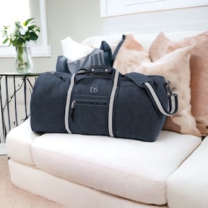 Puede incluir: Una bolsa de lona azul oscuro con rayas blancas y un bolsillo con cremallera. La bolsa tiene un monograma "DS" en la parte delantera.