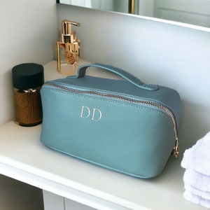 May include: A light blue toiletry bag with a gold zipper and handle. The bag has the initials "DD" embroidered on the front.