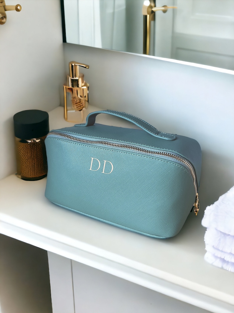 May include: A light blue toiletry bag with a gold zipper and handle. The bag has the initials "DD" embroidered on the front.