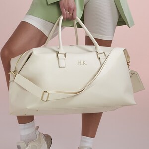 May include: A white leather duffel bag with gold hardware and a gold monogram "H.K." on the front.