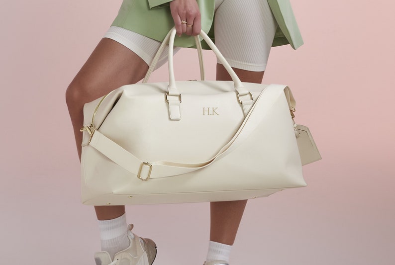 May include: A white leather duffel bag with gold hardware and a gold monogram "H.K." on the front.