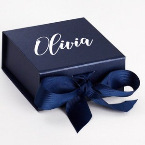 K&ouml;nnte beinhalten: Eine dunkelblaue Geschenkbox mit einem wei&szlig;en Band und dem Namen "Olivia" auf der Oberseite.