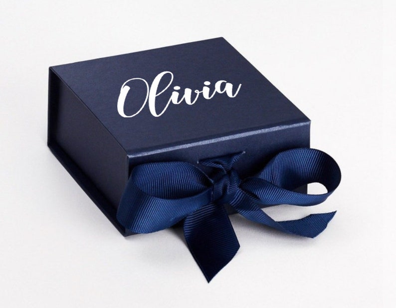K&ouml;nnte beinhalten: Eine dunkelblaue Geschenkbox mit einem wei&szlig;en Band und dem Namen "Olivia" auf der Oberseite.