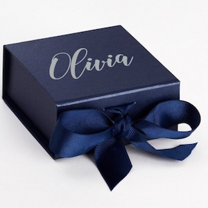 K&ouml;nnte beinhalten: Eine dunkelblaue Geschenkbox mit einem silbernen, gepr&auml;gten Namen "Olivia" und einem dunkelblauen Satinband.