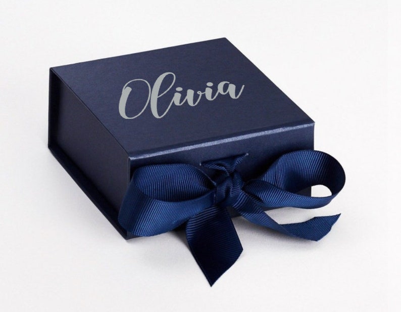 K&ouml;nnte beinhalten: Eine dunkelblaue Geschenkbox mit einem silbernen, gepr&auml;gten Namen "Olivia" und einem dunkelblauen Satinband.