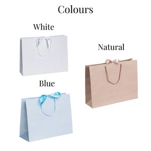 May include: Three paper gift bags with ribbon handles. The bags are white, blue, and natural brown. The text "Colours" is at the top of the image. The words "White", "Blue", and "Natural" are below each bag.