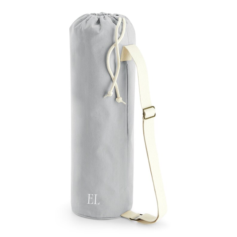 May include: A gray canvas yoga mat bag with a white drawstring and a white adjustable strap. The bag has the initials "EL" embroidered on the front.