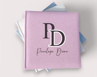 May include: A pink linen-covered photo album with the initials "PD" in black and white, and the name "Penelope Dixon" written in black cursive.