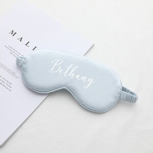 以下が含まれることがあります： 前面に白で「Bethany」と刺繍された薄い青色のアイマスクです。