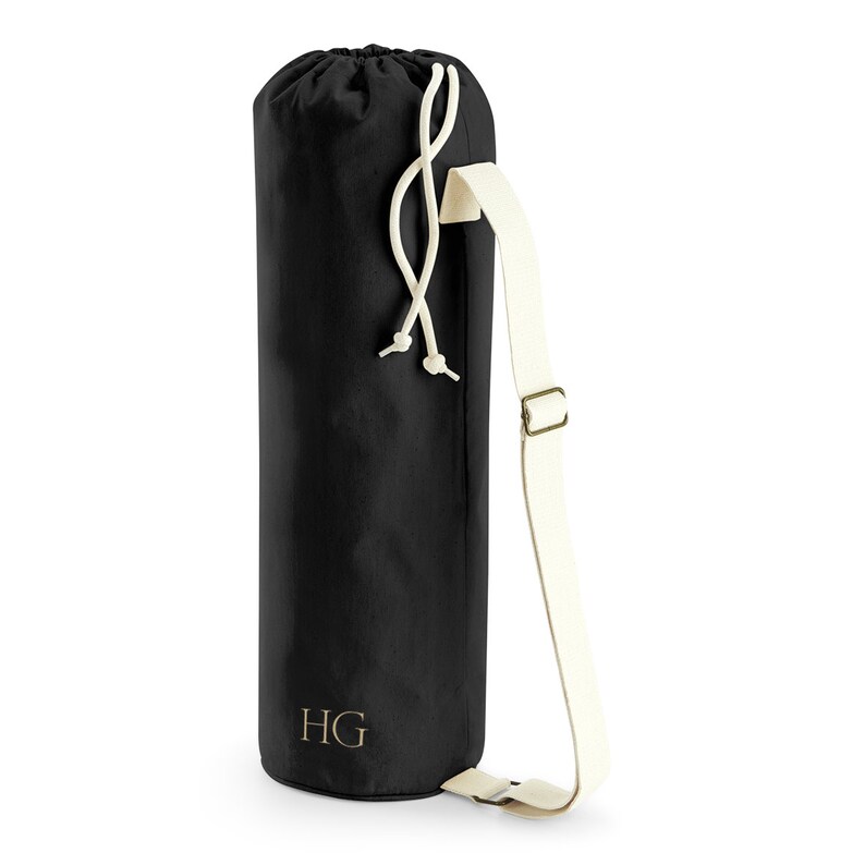 May include: Black yoga mat bag with a white drawstring and adjustable strap. The bag has a gold monogram "HG" on the front.